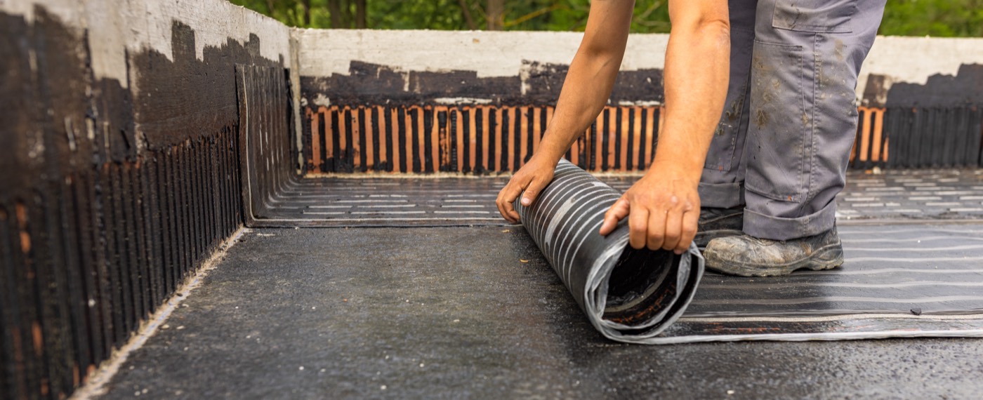 A worker applying a waterproofing membrane to a concrete foundation surface